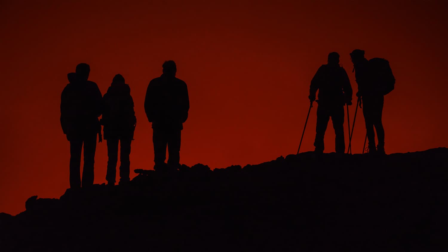 Silhouettes of trekkers standing against the red glow of the Erta Ale crater at night