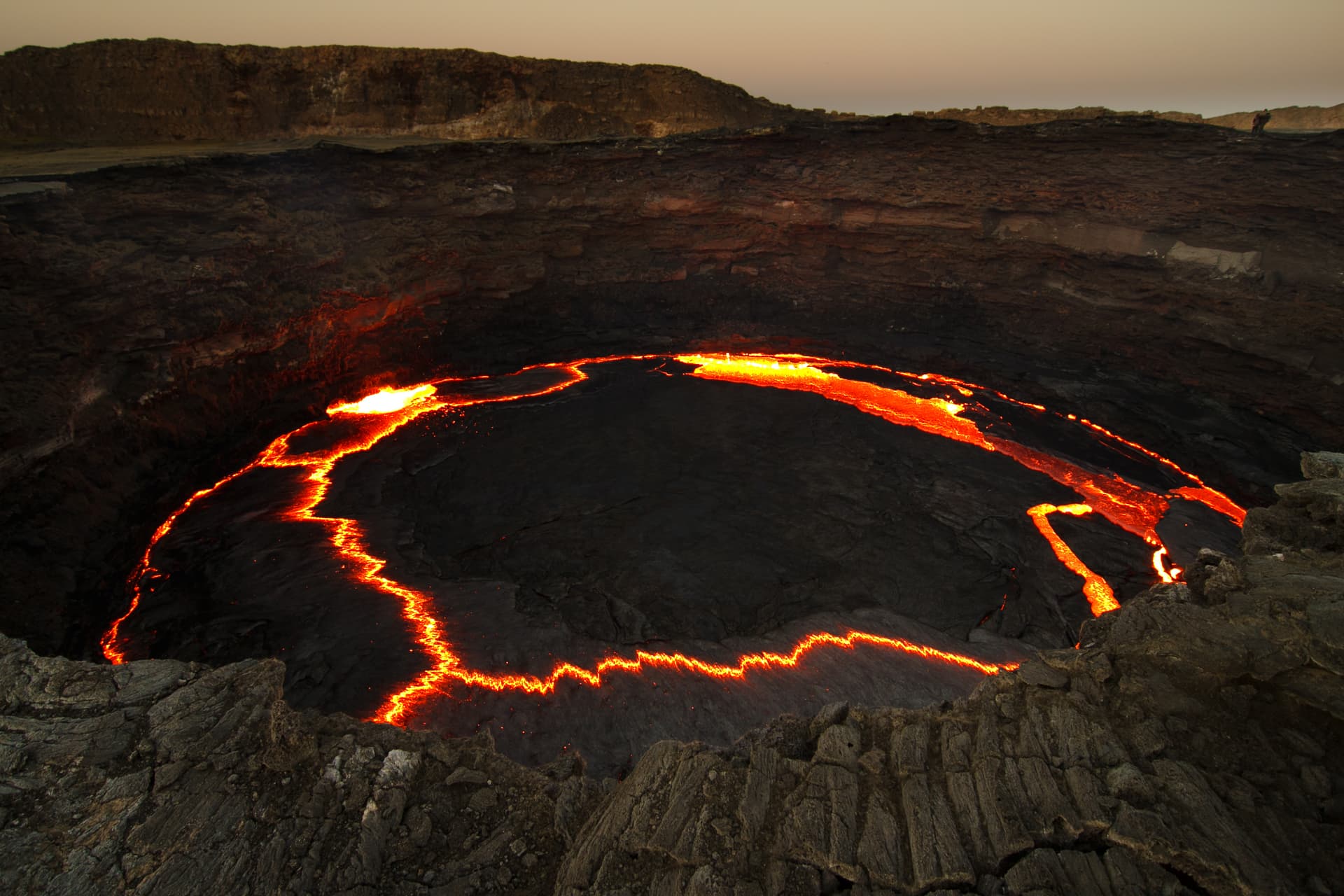 The Erta Ale lava lake at dusk, a black crust split by rivers of orange lava