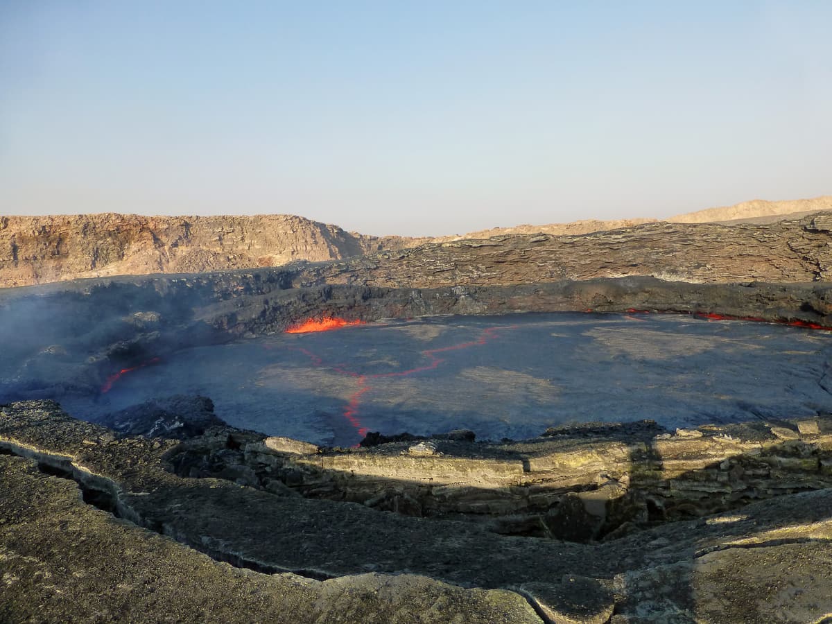 Dawn light over the Erta Ale caldera with a glowing lava pool below the crater wall
