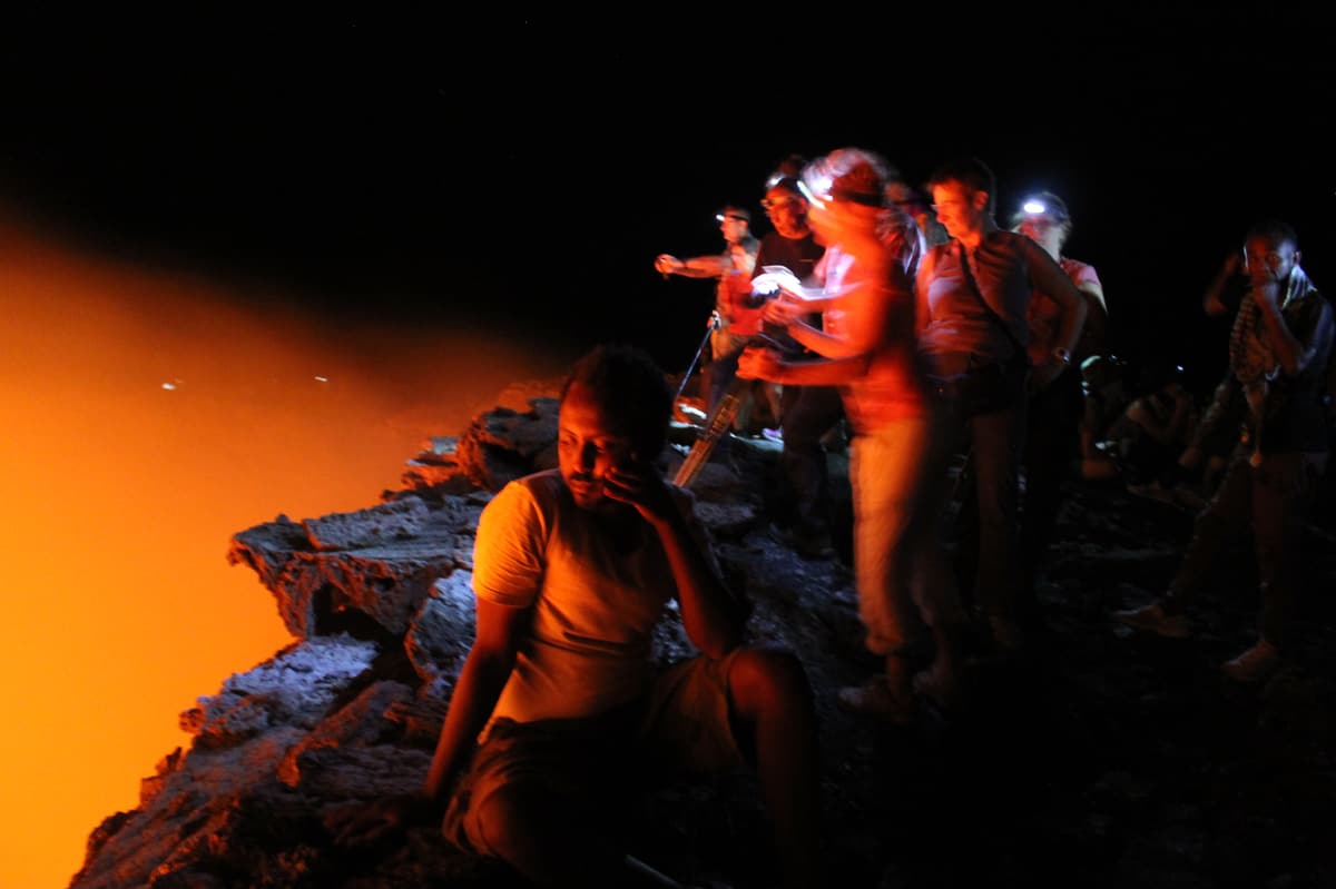 Trekkers with head torches resting on the dark lava rim of Erta Ale at night